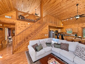 A spacious cabin with a wooden interior, a central living area with a sofa and coffee table, a kitchen with modern appliances, and a staircase connecting the floors.