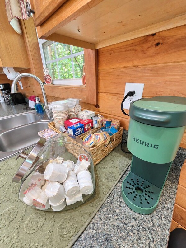 A kitchenette with a coffee maker, a basket of bread, and a glass container of milk cartons.