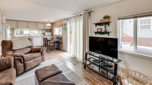 A cozy living room with a brown sofa, ottoman, and wicker chair, a flat-screen TV, and a dining area with a table and chairs. - Rockaway Beach Home, Walk to Ocean, Pet Friendly! (Rockaway Beach)