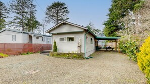 A single-story mobile home with a small porch and a covered outdoor area. - Rockaway Beach Home, Walk to Ocean, Pet Friendly! (Rockaway Beach)