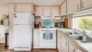 A compact kitchen with a refrigerator, stove, and double sink. - Rockaway Beach Home, Walk to Ocean, Pet Friendly! (Rockaway Beach)