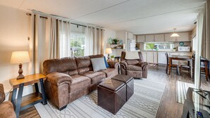 A living room with a brown leather sofa, a wooden coffee table, and a dining area with a table and chairs. - Rockaway Beach Home, Walk to Ocean, Pet Friendly! (Rockaway Beach)