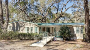A single-story house with a green roof, a front porch, and a small staircase leading to the entrance. - Work, Play & Explore! Retreat w/ Deck in McAlpin (McAlpin)