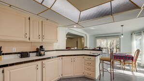 A kitchen with beige cabinets, a black countertop, and a dining area with a table and chairs. - Work, Play & Explore! Retreat w/ Deck in McAlpin (McAlpin)