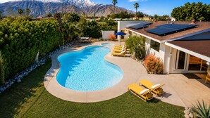 Piscina con montañas al fondo, paneles solares y una casa moderna.