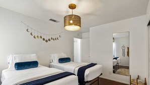 Un dormitorio con dos camas, una lámpara colgante, un espejo y una guirnalda de adornos con forma de luna.