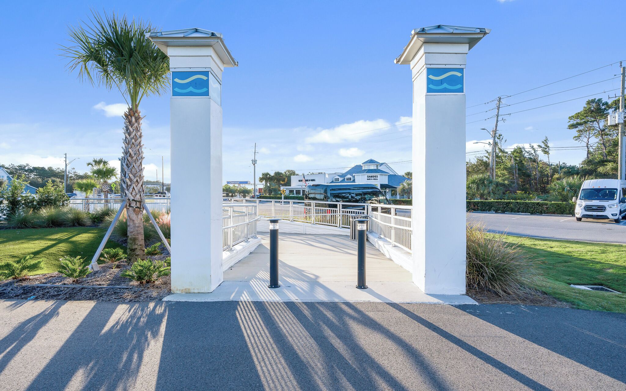 A gated entrance with two white pillars and a pedestrian bridge leading to a building with a blue roof.