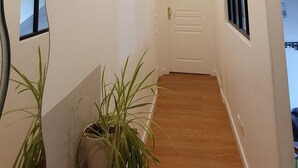 A hallway with a wooden floor, a white door at the end, and a potted plant on a wooden bench.