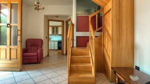 A spacious room with a wooden staircase, a red chair, and a kitchen visible through an open door.