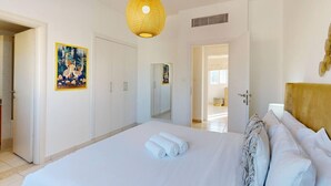 Hotellihuone, jossa on suuri sänky, riippuvalaisin, taulu seinällä ja ovi, joka johtaa toiseen huoneeseen.