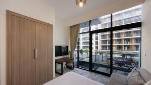 Habitación de hotel con una cama grande, un escritorio con televisor, un balcón con vistas a un edificio moderno y un armario.