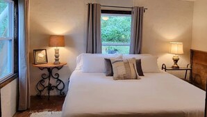 Un dormitorio con una cama, dos mesitas de noche con lámparas, un ventilador de techo y una ventana con cortinas.
