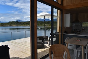 A modern kitchen with a large window, a dining area with a table and chairs, and a view of a lake with mountains in the background.