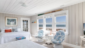 Una camera da letto con due letti, una finestra vista spiaggia e una sedia con un cuscino decorativo.