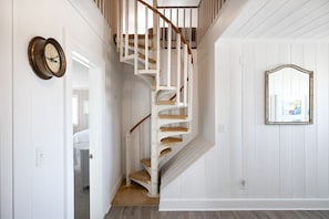 A spiral staircase with white railings and a wooden handrail, leading to an upper floor.