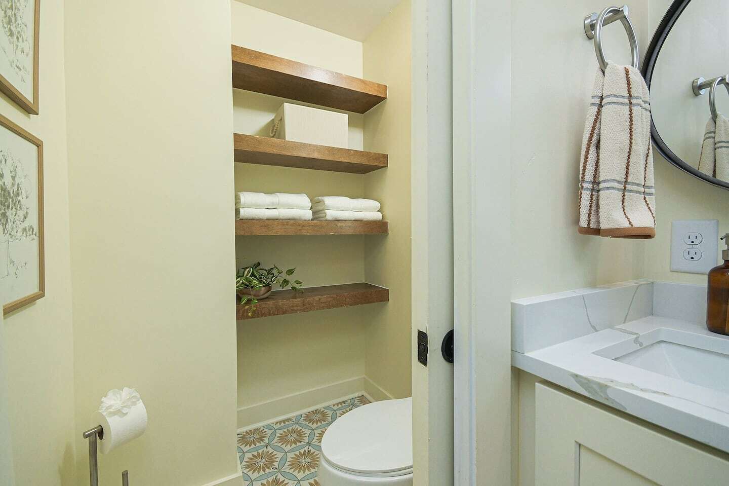 Une salle de bain équipée de toilettes, d’un lavabo, d’un miroir et d’étagères où sont rangées les serviettes.