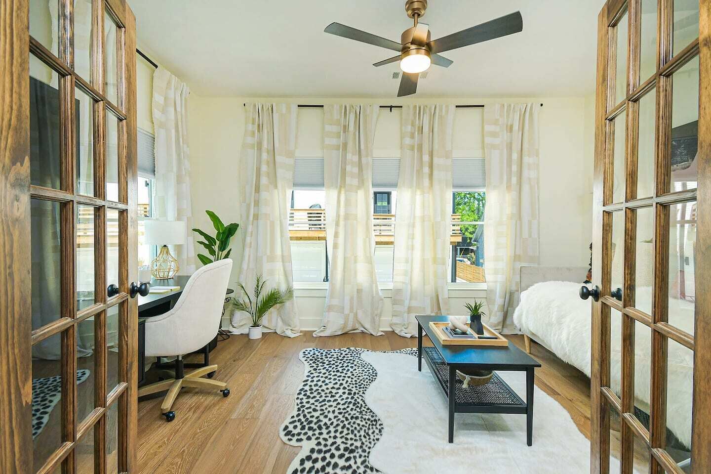 A modern bedroom with a desk, chair, bed, and a ceiling fan.