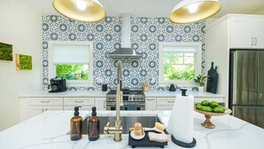 Una cucina moderna con isola centrale, due luci a sospensione, zoccolo paraschizzi decorato e frigorifero in acciaio inossidabile.