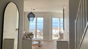 Ein großzügiger Wohnbereich mit großem Fenster und Meerblick, einer modernen Chandelüster und einem minimalistischen Design.