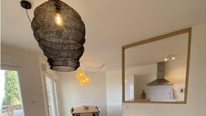 Ein modernes Wohnzimmer mit einer Couch, einem runden Holztisch mit einer Vase, einer Hängeleuchte und einem großen Spiegel an der Wand.