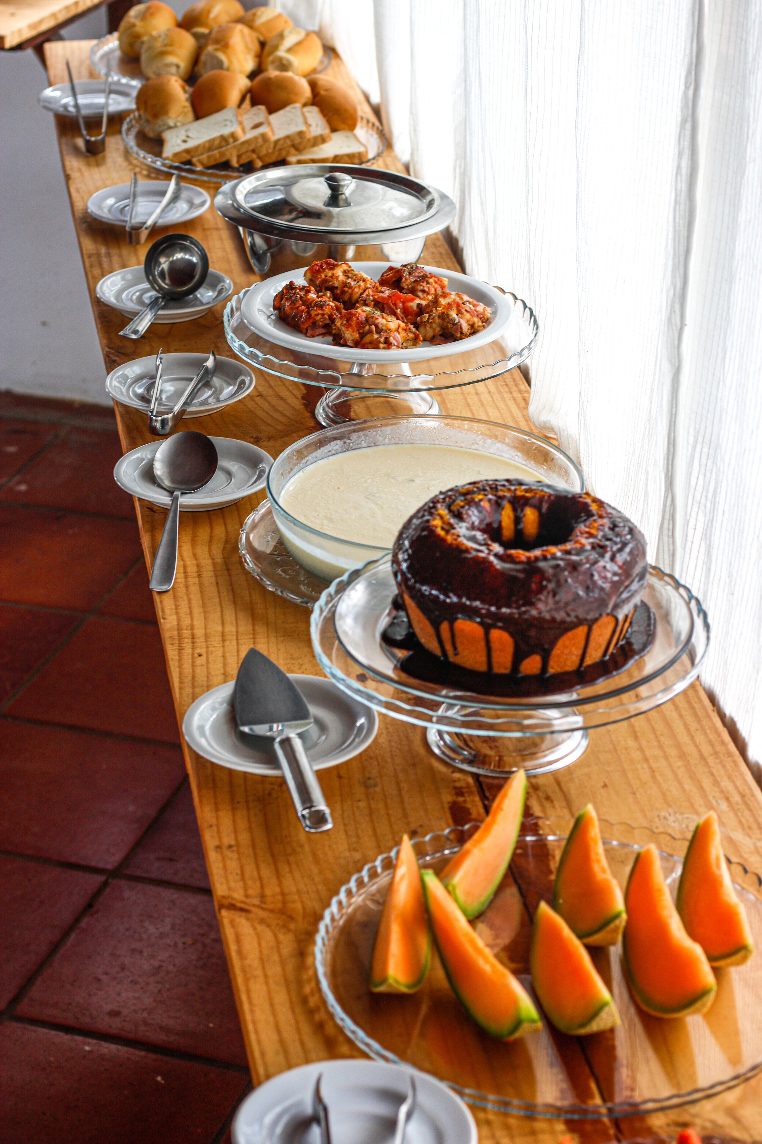 A buffet table with various food items including bread, a chocolate cake, and sliced fruits.