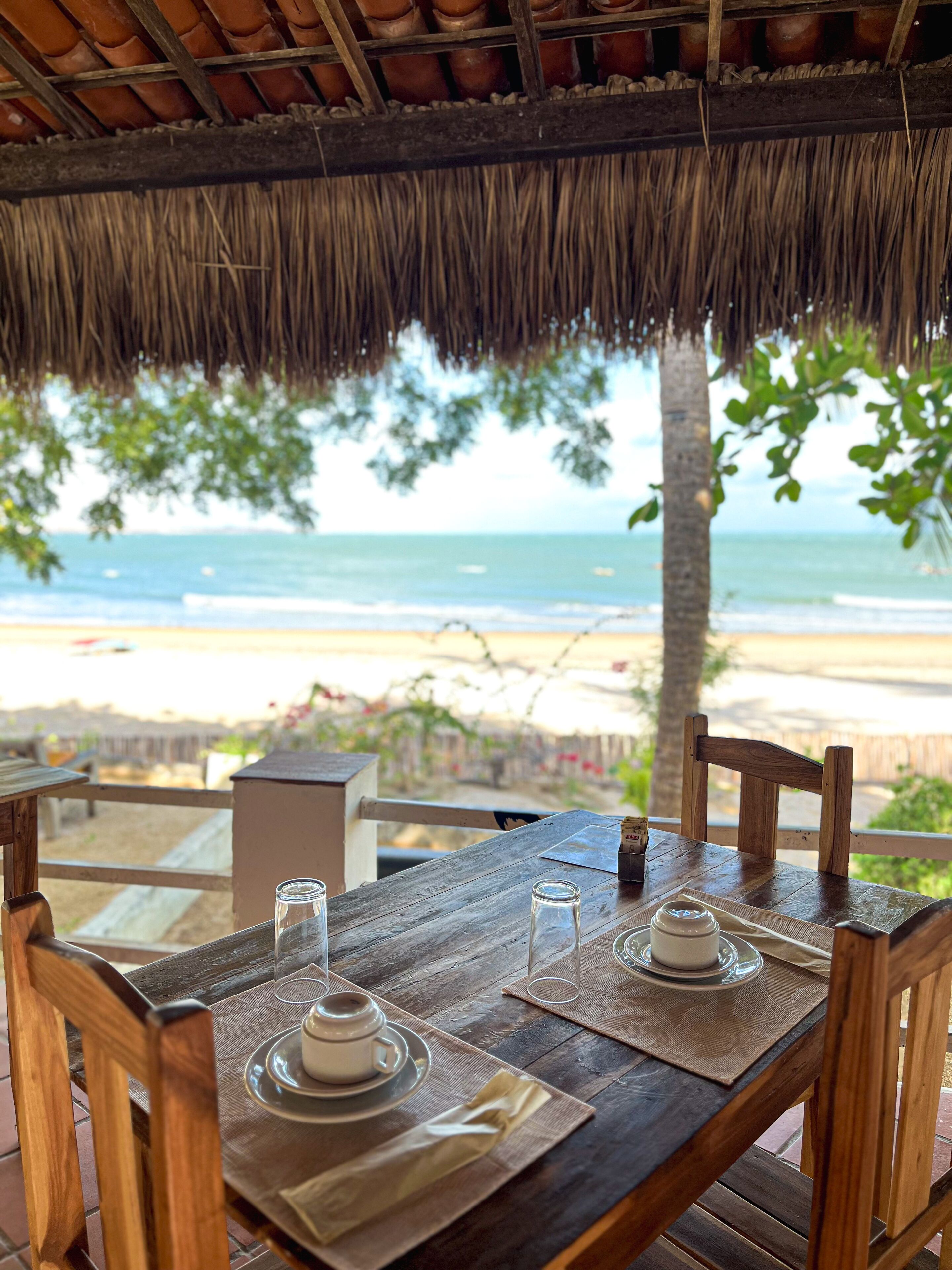 A wooden table set for two with a view of the beach and ocean.