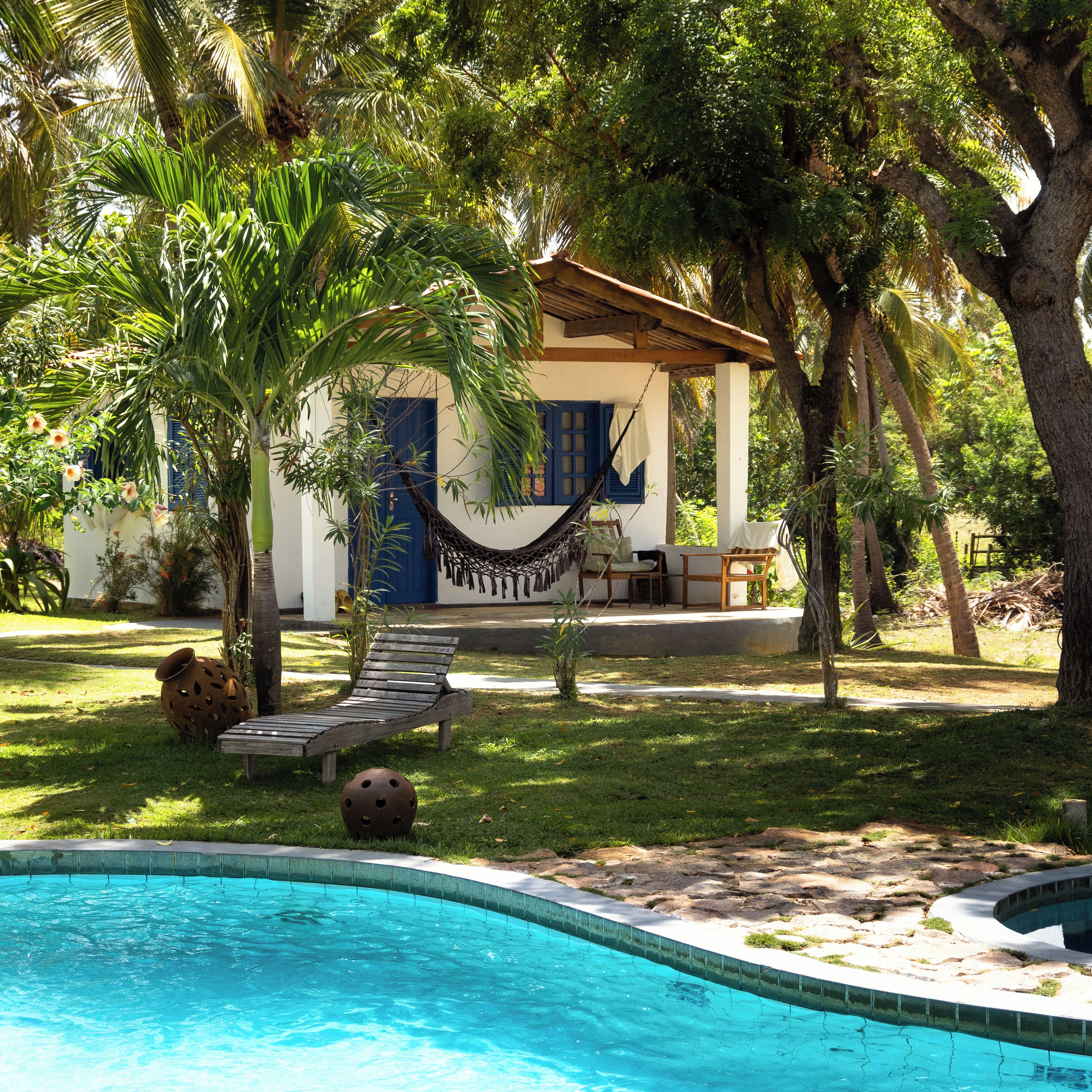 A pool area with a hammock, lounge chairs, and a small house with a blue door.