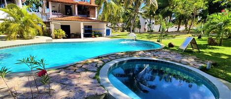 Una piscina con borde de piedra, un jacuzzi pequeño y una zona de recepción con balcón.