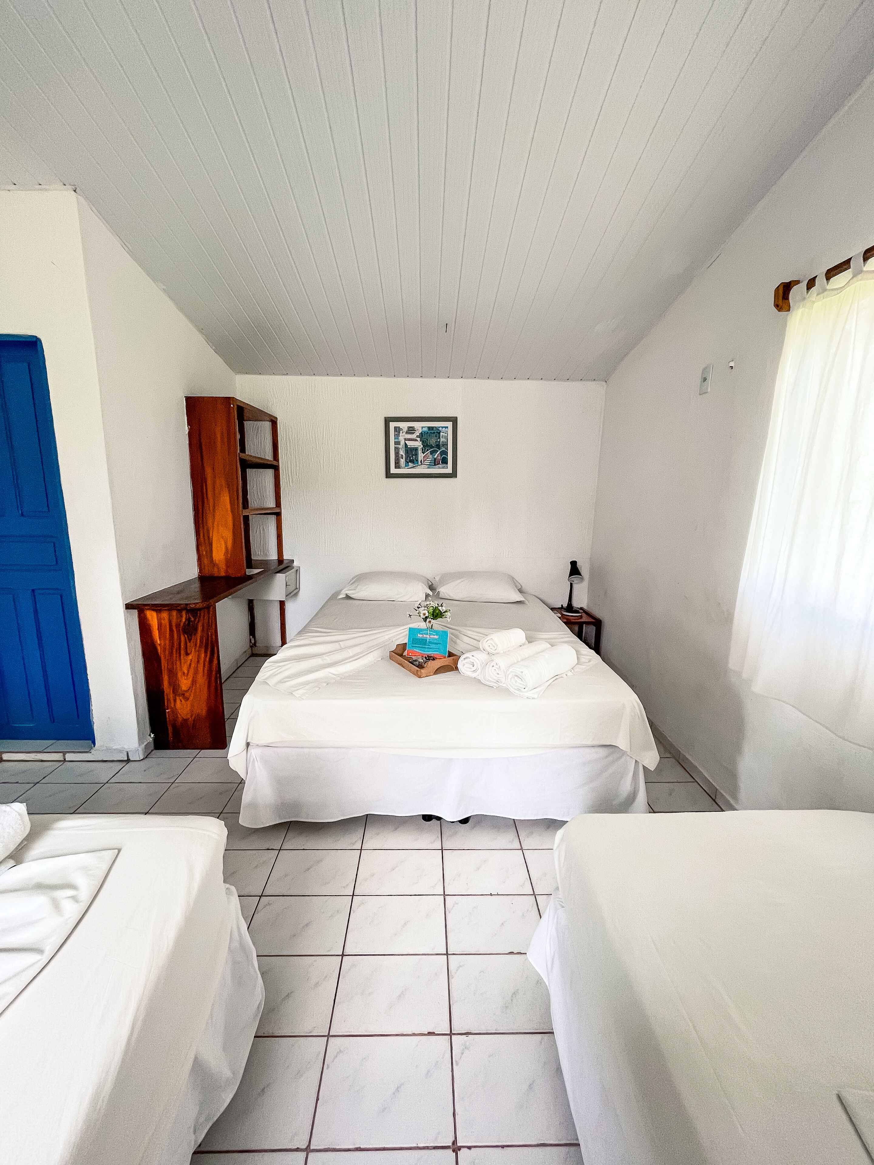A room with a bed, a small wooden cabinet, a framed picture on the wall, and a blue door.
