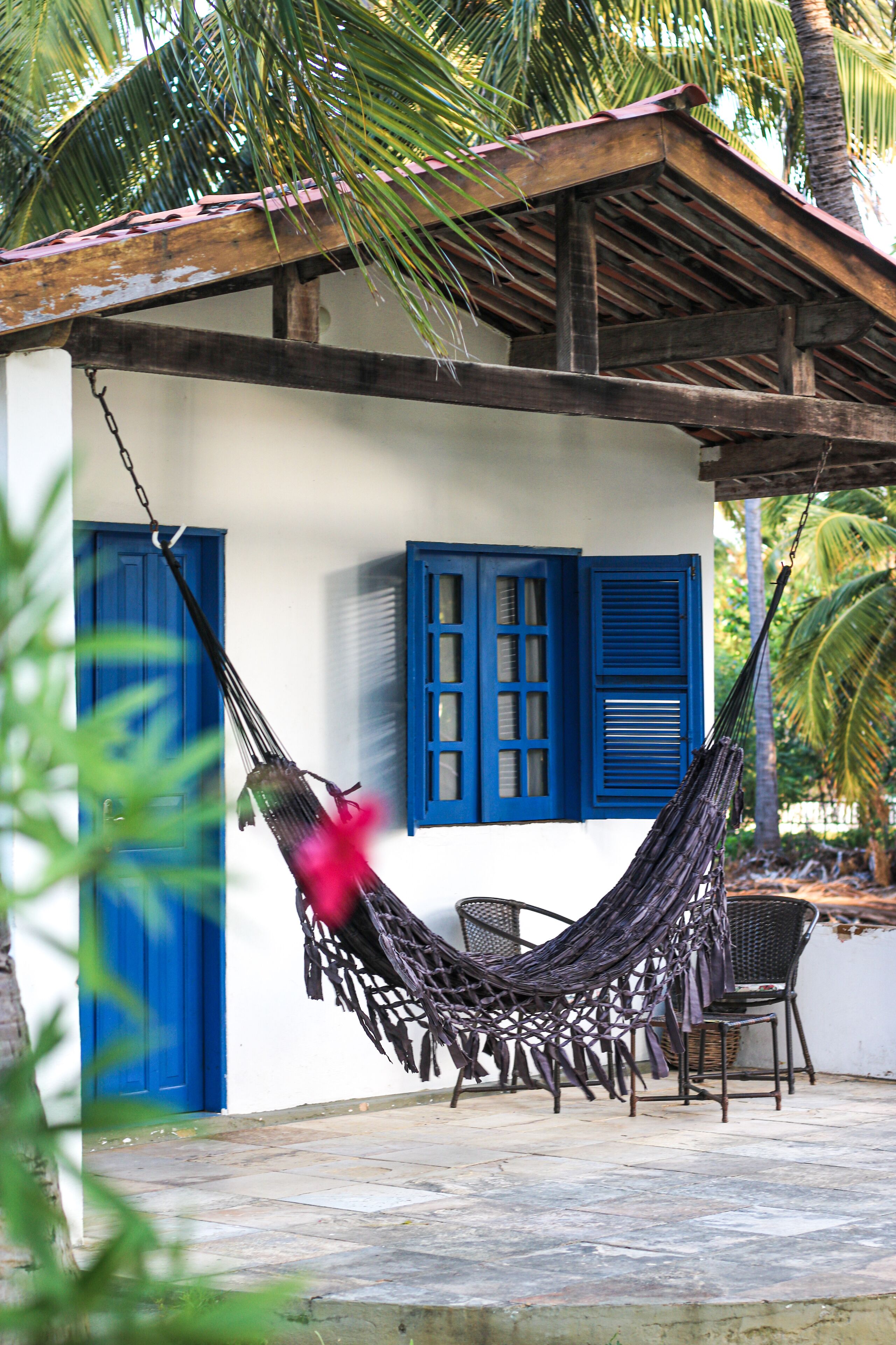 A hammock tied between two chairs, a small table, and a blue door.