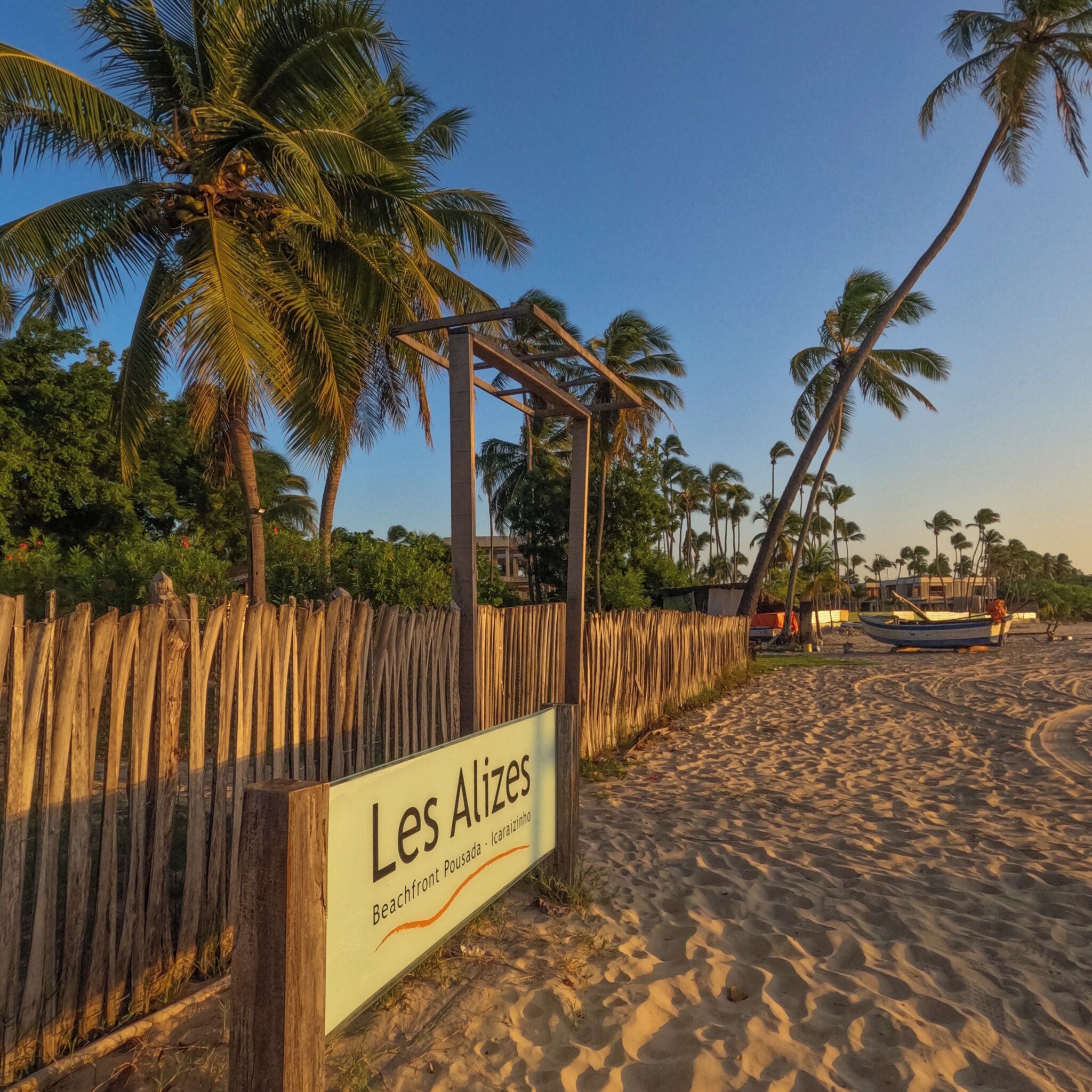 A beach with a wooden fence and a sign that reads "Les Alizes Beachfront Pousada - Icaraizilí".