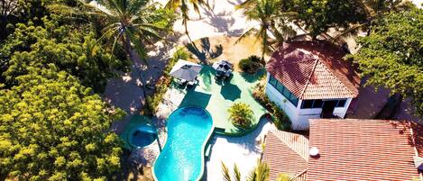 An aerial view of a property with a swimming pool, outdoor seating, and a building with a tiled roof.