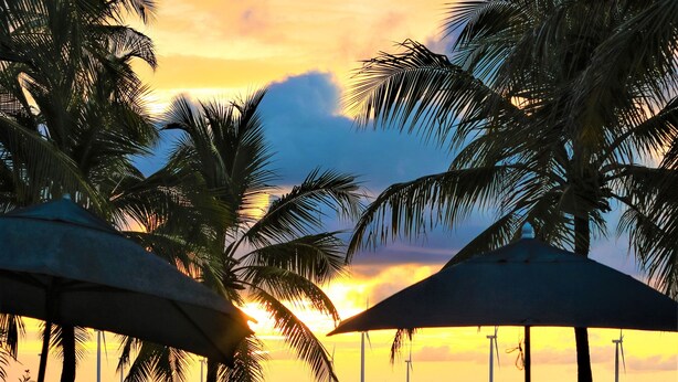 A poolside area with lounge chairs and umbrellas, overlooking a body of water and palm trees during sunset. - Pousada Les Alizes (Amontada)