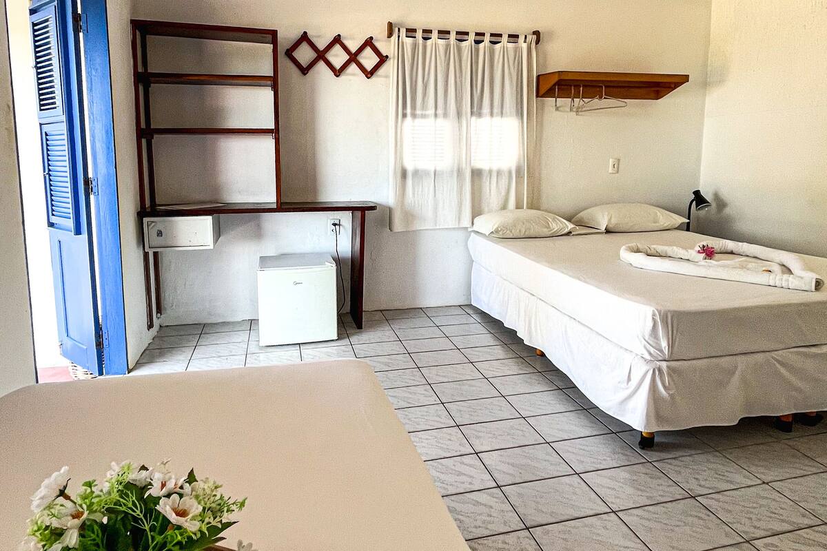 Un dormitorio con cama, escritorio, silla, mesita de noche y ventana con cortinas.