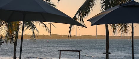 A poolside area with umbrellas, benches, and a view of the ocean.