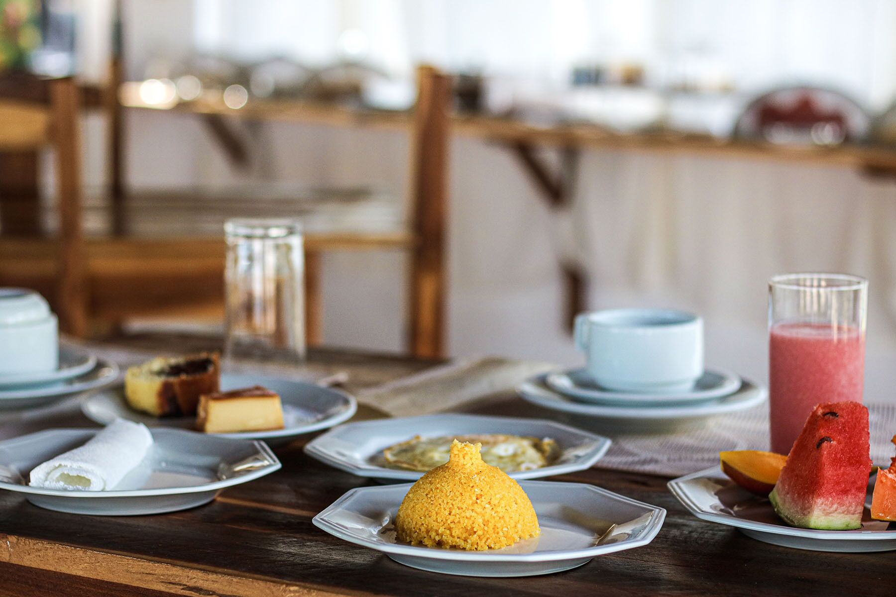 A dining table with various dishes, including a yellow dessert, watermelon, and a pink drink.