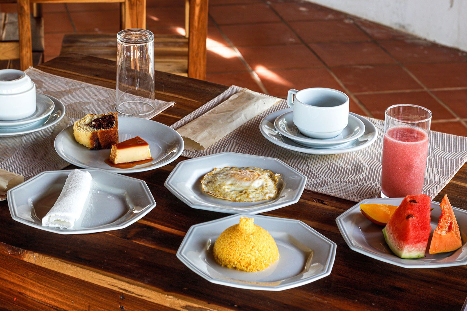 A table set with various dishes including a slice of cake, a fruit salad, and a glass of smoothie.