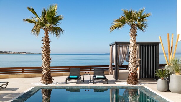 Zona junto a la piscina con dos tumbonas, una mesita y un espacio para sentarse con vista al mar.