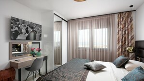 Habitación de hotel moderna con cama, escritorio, silla, espejo grande y televisión.