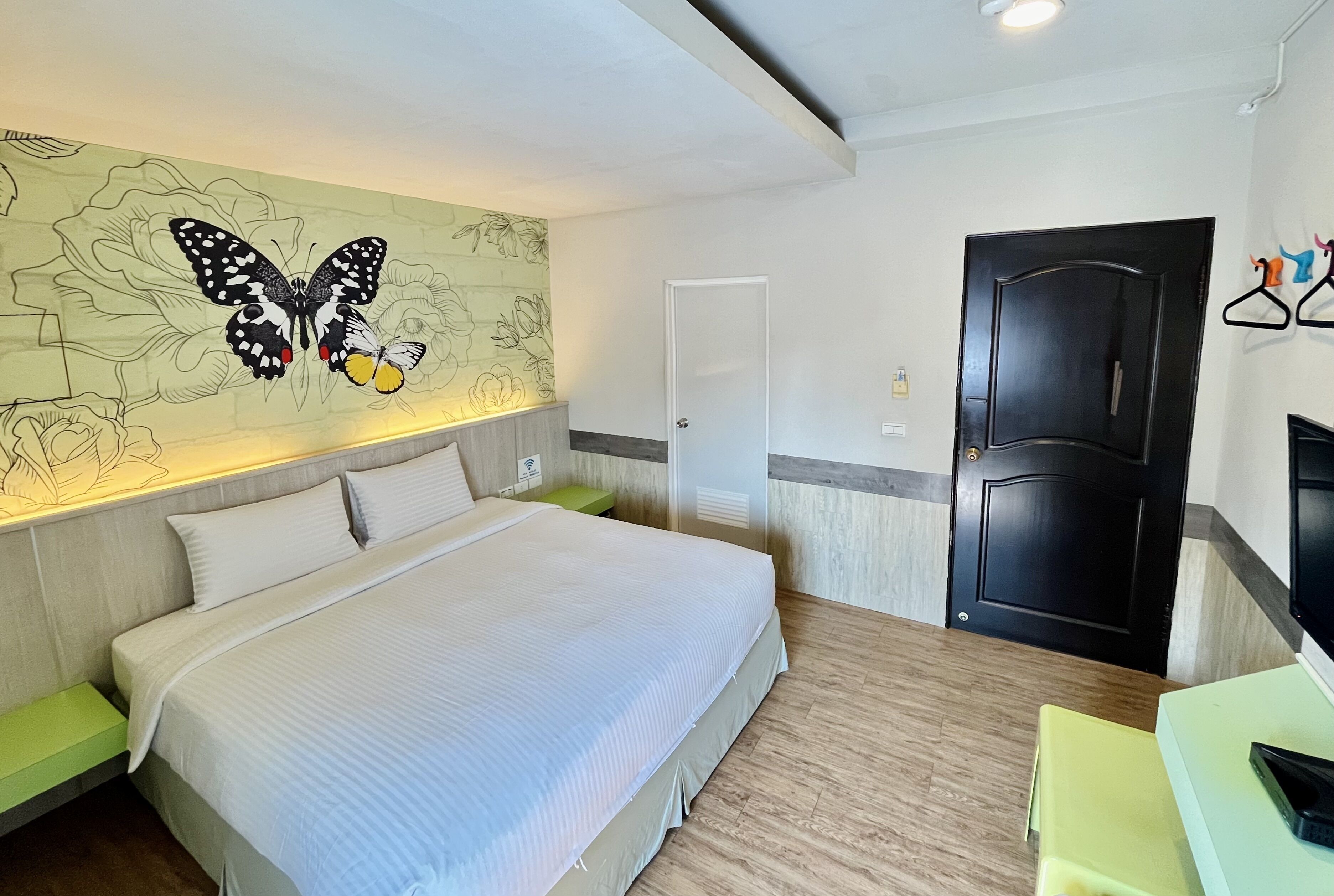 A hotel room with a bed, a green bench, a wall with a butterfly mural, a wardrobe, and a door.