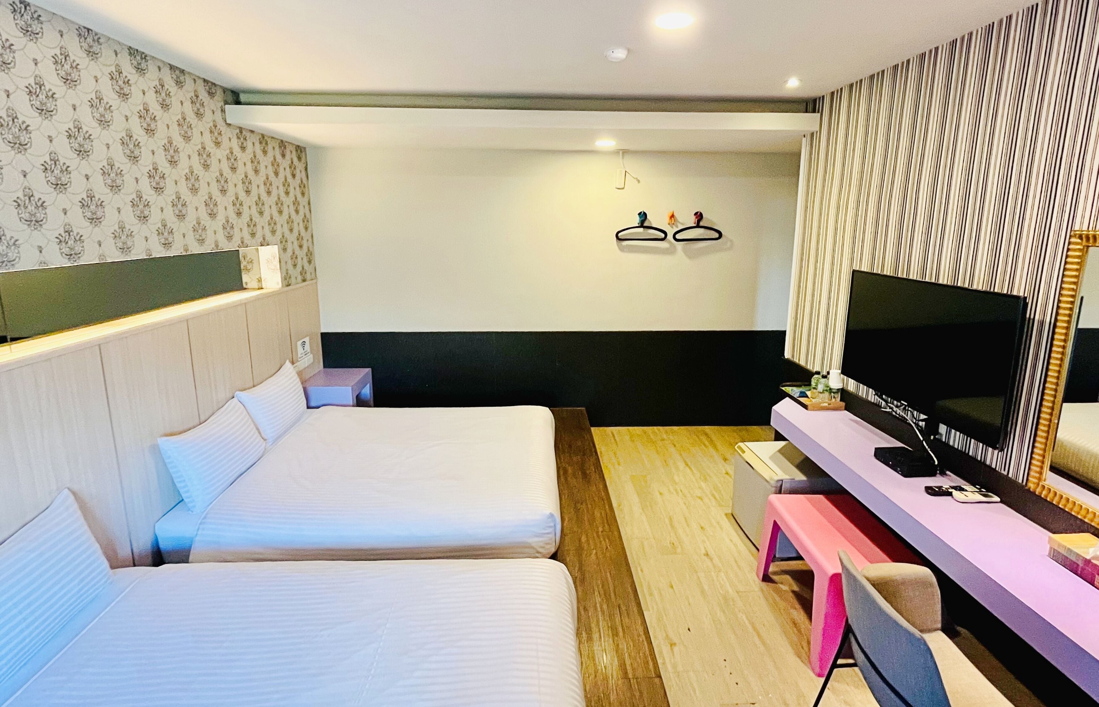 A hotel room with two beds, a TV, a bench, and a mirror.