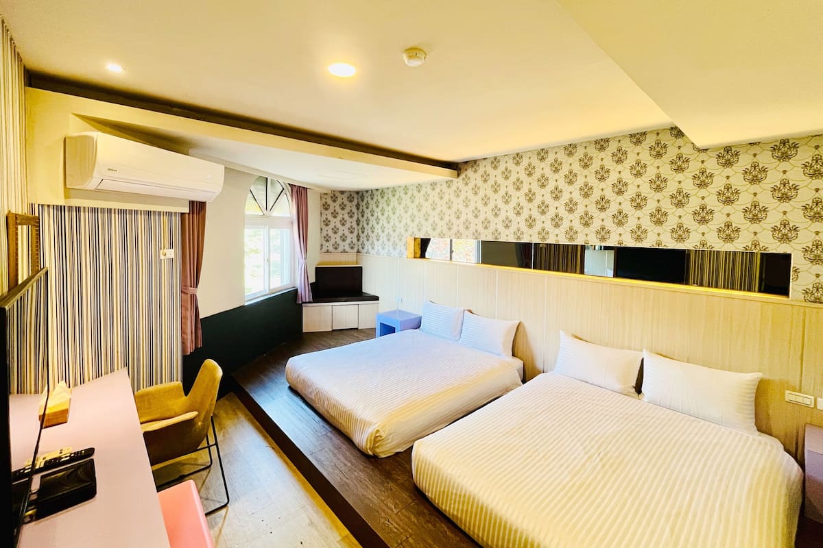 A hotel room with two beds, a desk, a chair, a TV, and an air conditioning unit.