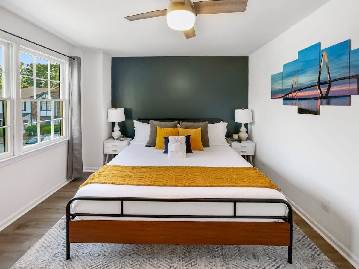 A modern bedroom with a bed, nightstands, a ceiling fan, and a large window.