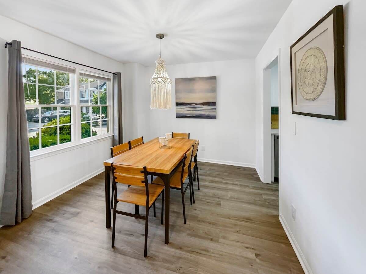 Een eetruimte met een houten tafel en stoelen, een hanglamp en een schilderij aan de muur.