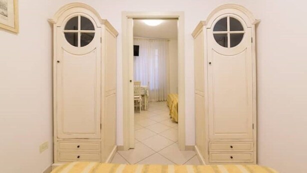 A hallway with two tall wardrobes and a bed with a striped bedspread.