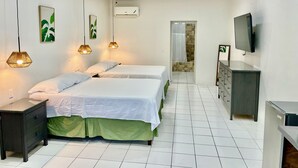 Quarto com duas camas, televisão, penteadeira e banheiro visível por uma porta aberta.