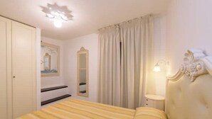 A bedroom with a bed, a mirror, a nightstand, and a window with curtains. - Carla House - Monterosso Cinque Terre .- Citra011019-LT-0135 (Monterosso al Mare)