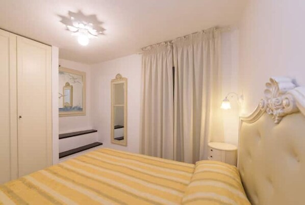 A bedroom with a bed, a mirror, a nightstand, and a window with curtains.