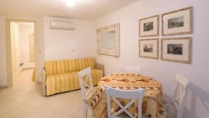 A small, well-lit room with a striped sofa, a round table with chairs, and framed pictures on the wall. - Carla House - Monterosso Cinque Terre .- Citra011019-LT-0135 (Monterosso al Mare)