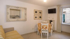 A compact living space with a dining area, a sofa, a television, and a window with curtains. - Carla House - Monterosso Cinque Terre .- Citra011019-LT-0135 (Monterosso al Mare)